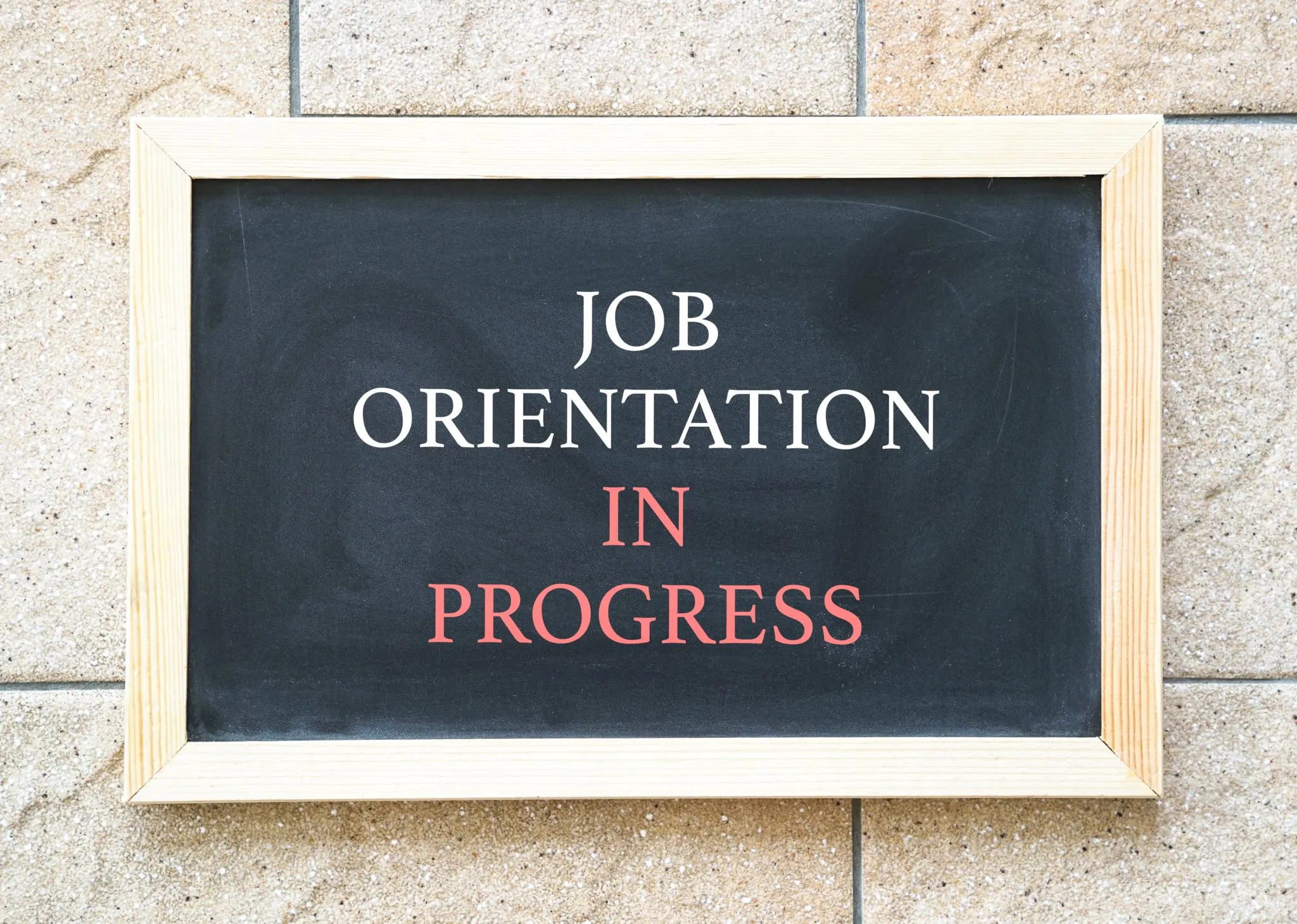 A chalkboard sign displaying the text framed in wood, against a textured stone wall